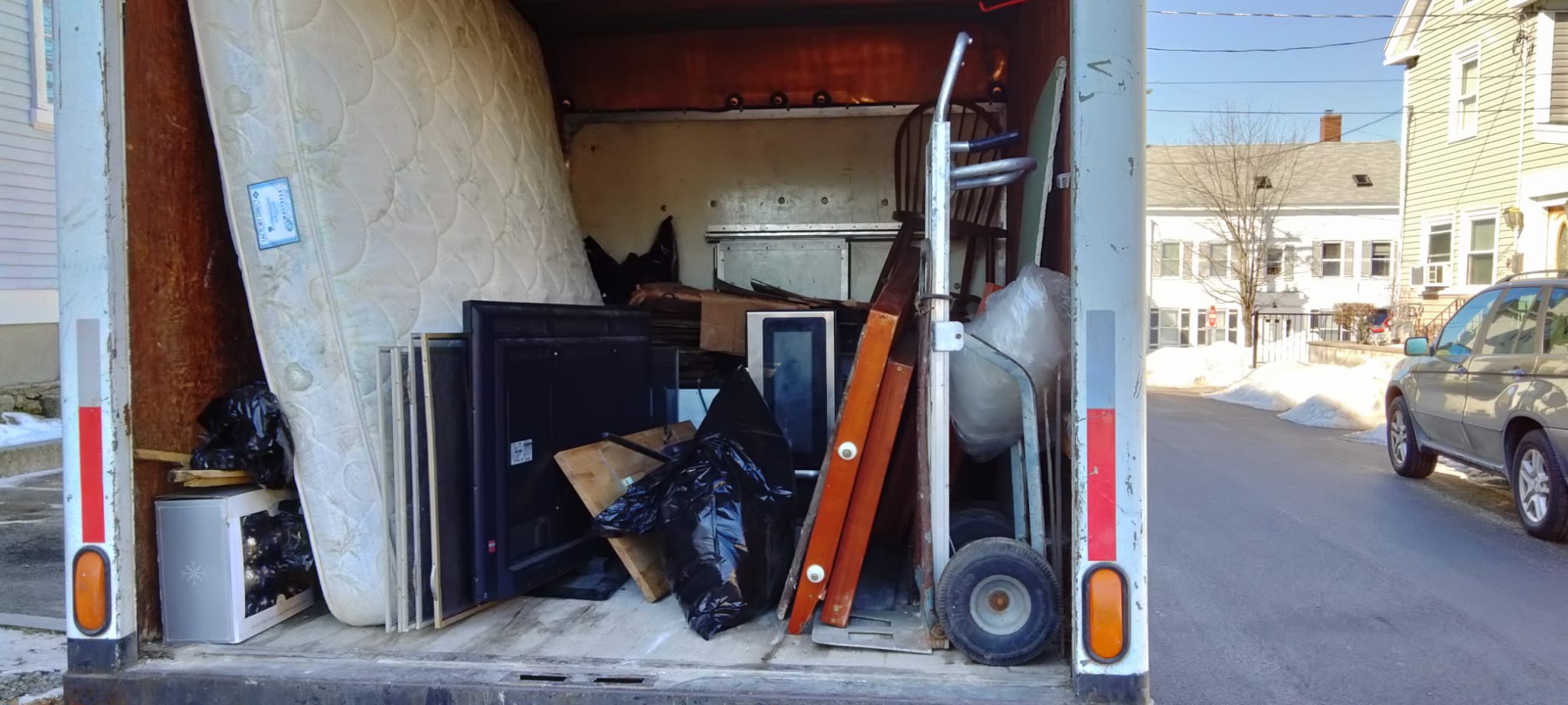 Box truck with old junk from an house in it, including a TV, a microwave, and a mattress