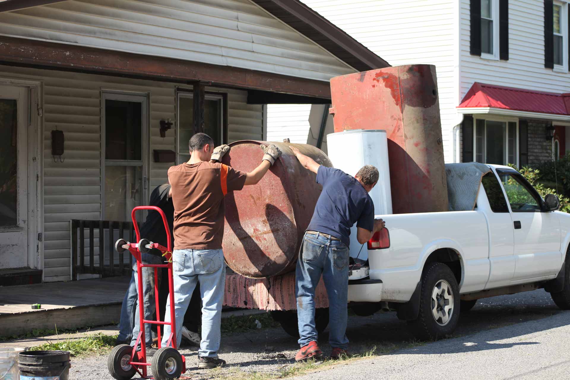 Two men loading scrap metal and an old hot water heater on to the back of a truck